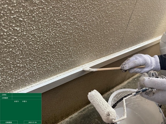 外壁下端の水切りを小さめのローラーで塗り分けている付帯部塗装の作業