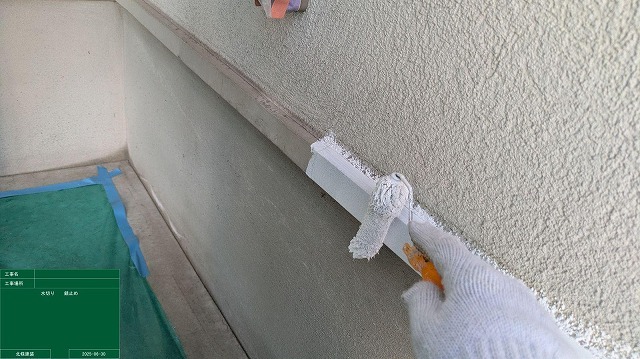 外壁下端の水切りに白い錆止め塗料をハケとローラーで塗り込む作業
