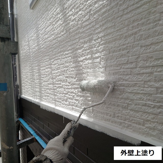 ベージュの上塗りを重ねている外壁上部