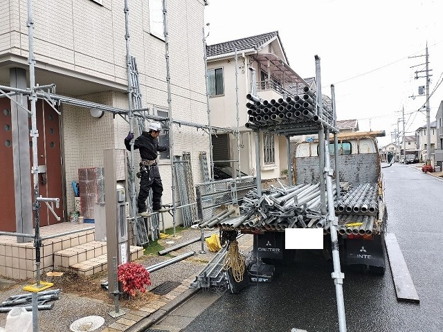 外壁塗装のために単管足場を組み立てている様子。資材を積んだトラックから部材を搬入