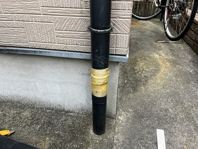 自転車の衝突で割れた黒い竪樋に応急処置のテープが巻かれた施工前の状態
