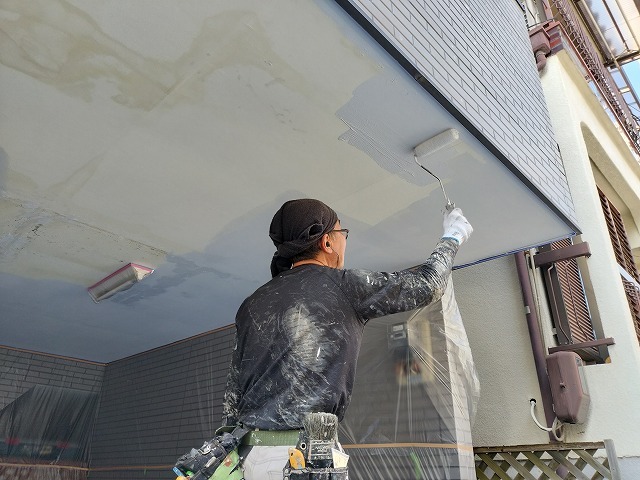 軒天の広い面をローラーで塗装している職人の作業風景