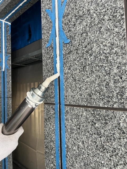 マスキングした目地に新しいシーリング材をコーキングガンで充填する作業